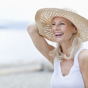 person on the beach smiling and wearing white dress and hat