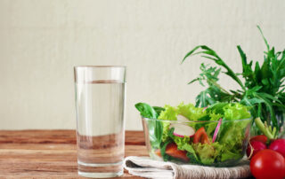 glass of water and bowl of vegetables sitting on a wooden table