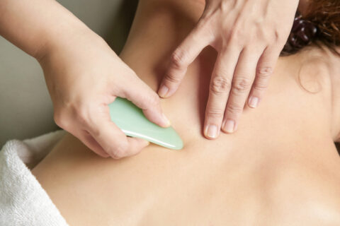 Person receiving gua sha treatment with pale blue stone tool