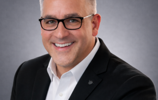 Headshot of Daniel Lalonde, COO of Red Leaf Wellness, wearing a white collared shirt and dark grey jacket on a grey background.