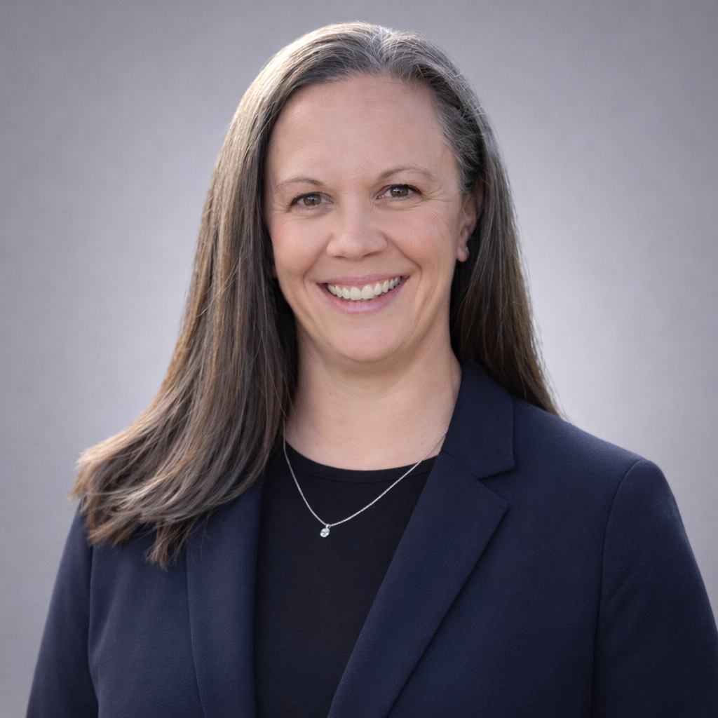 Headshot of Dr. Michelle Winton, Acupuncturist and RMT, smiling in a navy blazer against a neutral gray studio background.