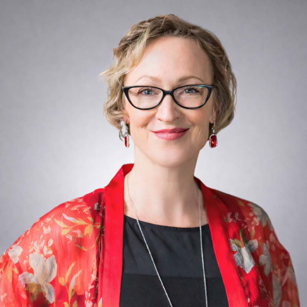Headshot of Dr. Ac. Tammy Lalonde, CEO, wearing black glasses and a red floral wrap over a black top, smiling against a soft gray background.