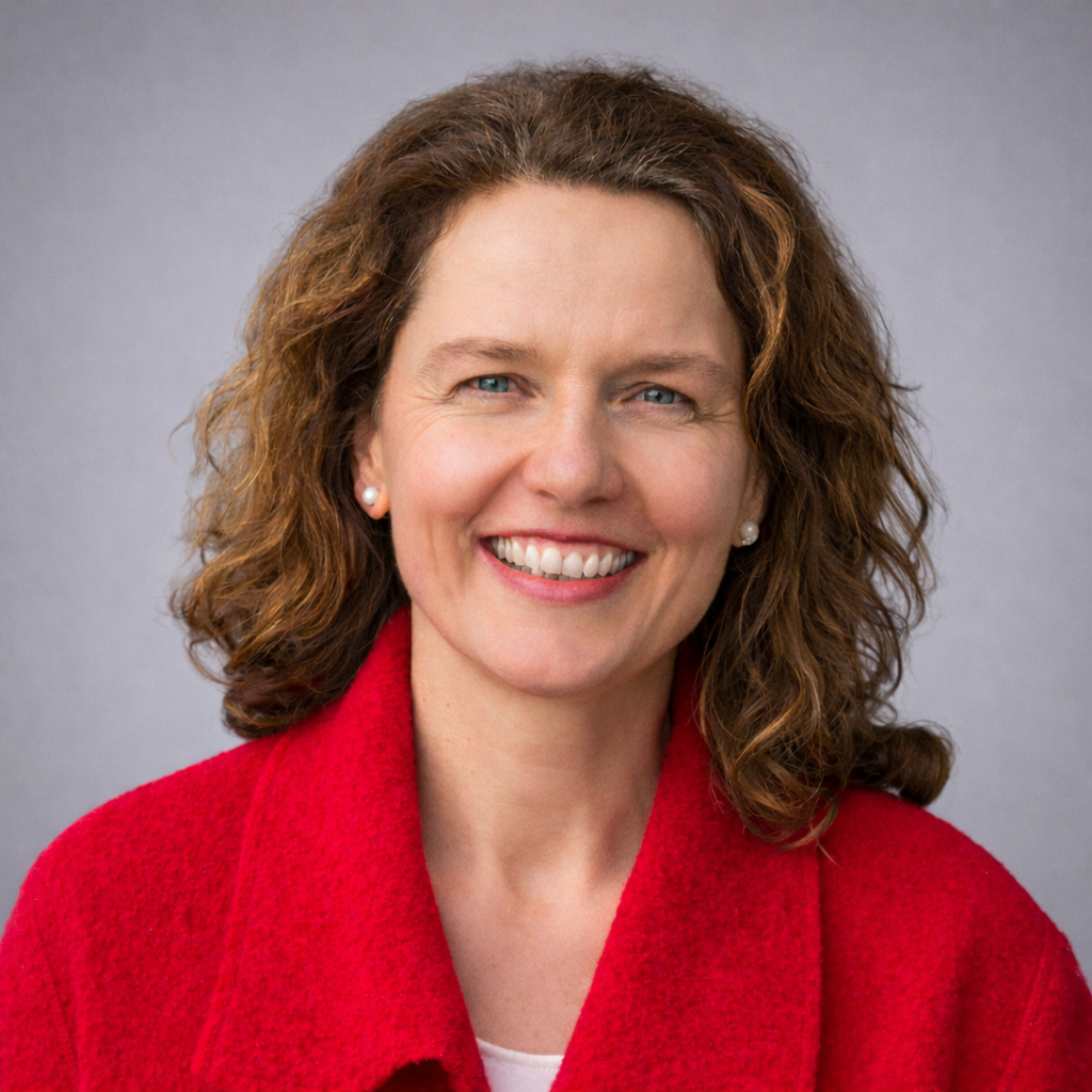 Headshot of Manuela Hofer, RMT and BCST, smiling in a red coat against a soft gray studio background.