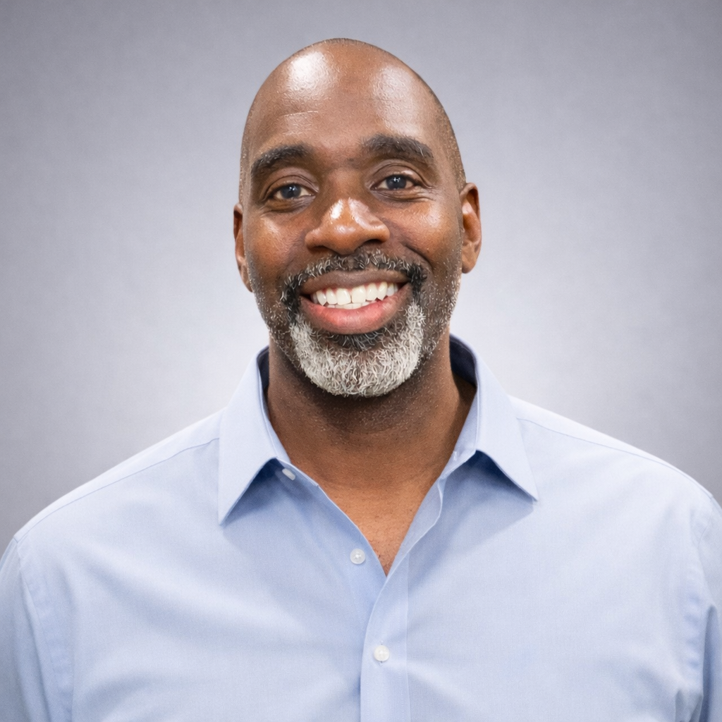 Headshot of Royston Frederick, Energy Medicine practitioner, smiling in a light blue dress shirt against a soft gray studio background.