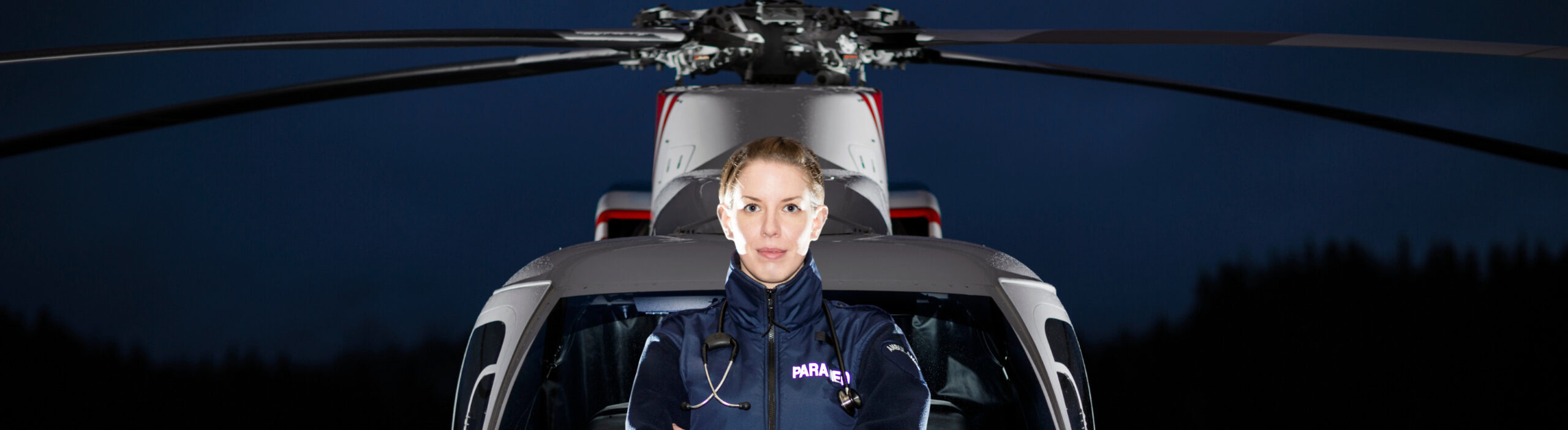 Female flight paramedic in front of a medical helicopter, arms crossed, offering PTSD treatment in Edmonton.