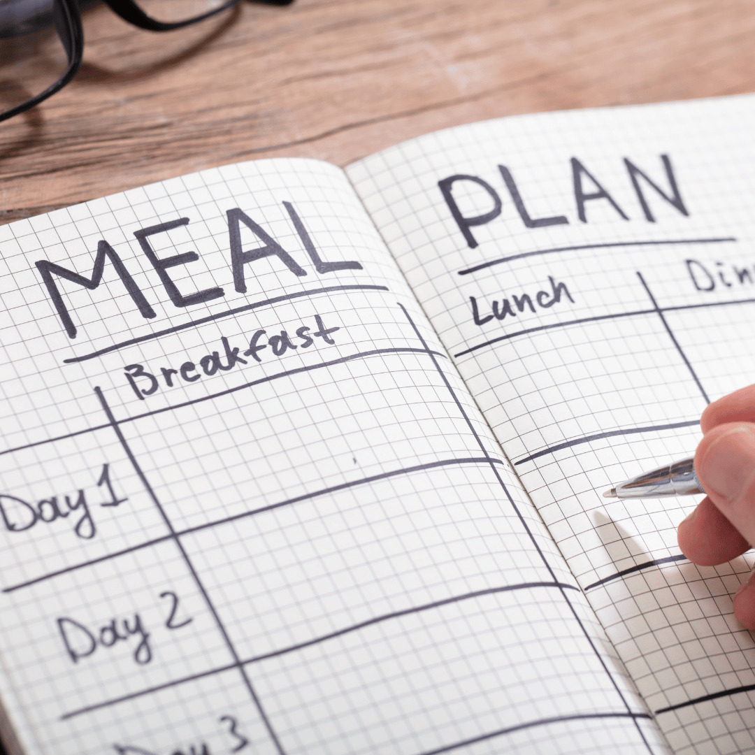Person holding a pen over a meal plan template, ready to make an entry, illustrating the custom meal planning services at Red Leaf Wellness in Edmonton.