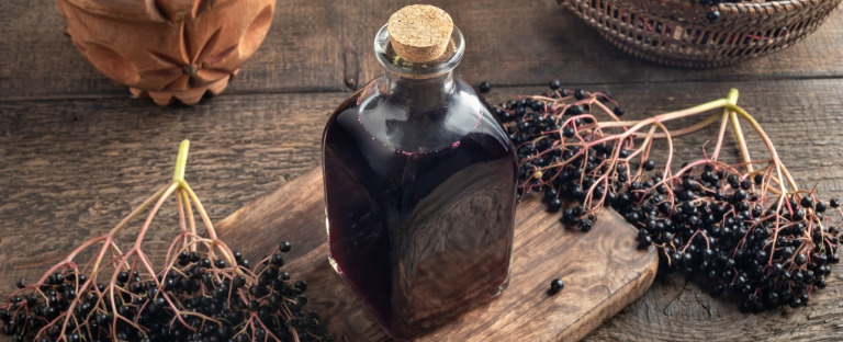 Elderberry vinaigrette in a glass bottle with a cork stopper, placed on a wooden cutting board on a wooden table, surrounded by elderberries