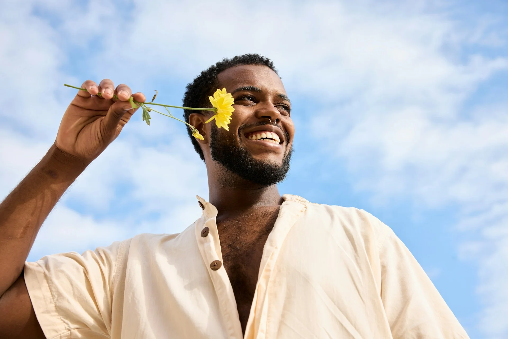 photo - a happy man holding up a flower to his face and smiling