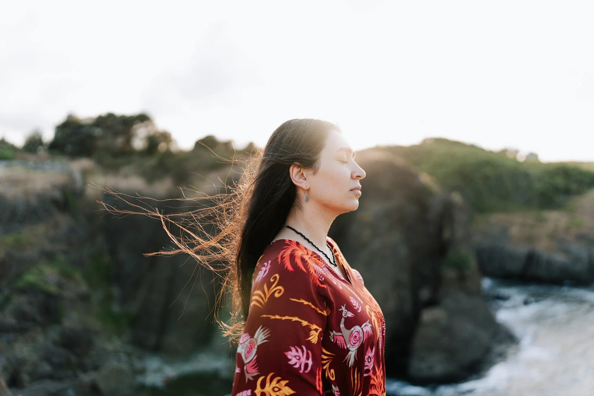 photo - a woman naturopath for women's health standing outdoors by the water with wind in her hair