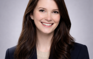 Headshot of Allie Kusnierczyk, Nurse Practitioner, smiling in a navy blazer against a soft gray studio background.