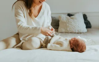 photo - a new mother playing with her newborn baby before her postpartum massage appointment