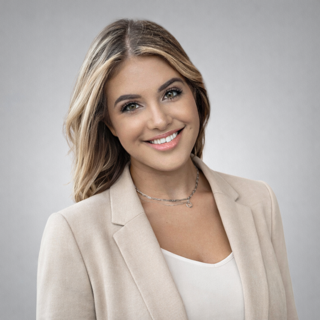 A friendly young woman with shoulder-length blonde hair, smiling warmly. She is wearing a light jacket and a delicate necklace, exuding approachability and professionalism. The background is a soft gray gradient.