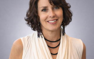 Headshot of Jennifer Steed, Registered Massage Therapist, smiling in an off white draped top against a soft gray studio background.