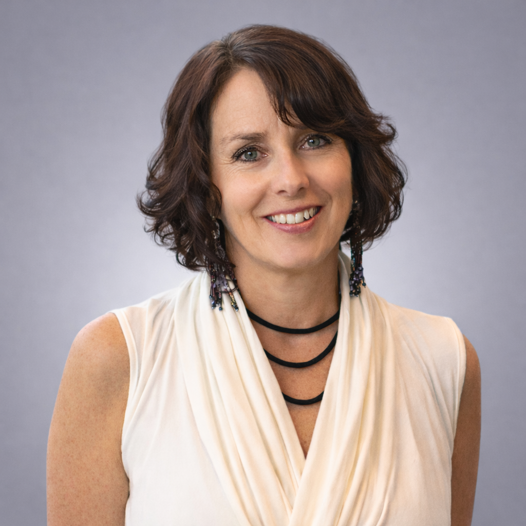 Headshot of Jennifer Steed, Registered Massage Therapist, smiling in an off white draped top against a soft gray studio background.