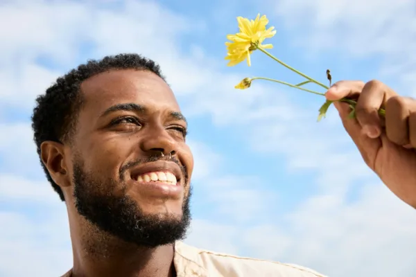 a man smiling at a yellow flowing in his hand