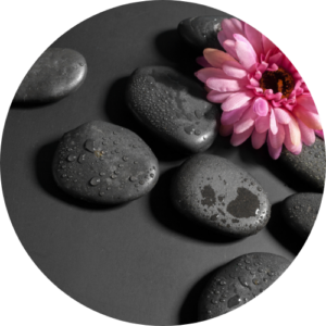 Smooth black hot stones placed on a spa bed with a pink flower beside them.