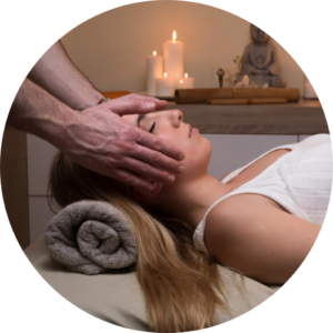 Therapist placing hands gently on a client’s head in a serene environment with candles and soft lighting.