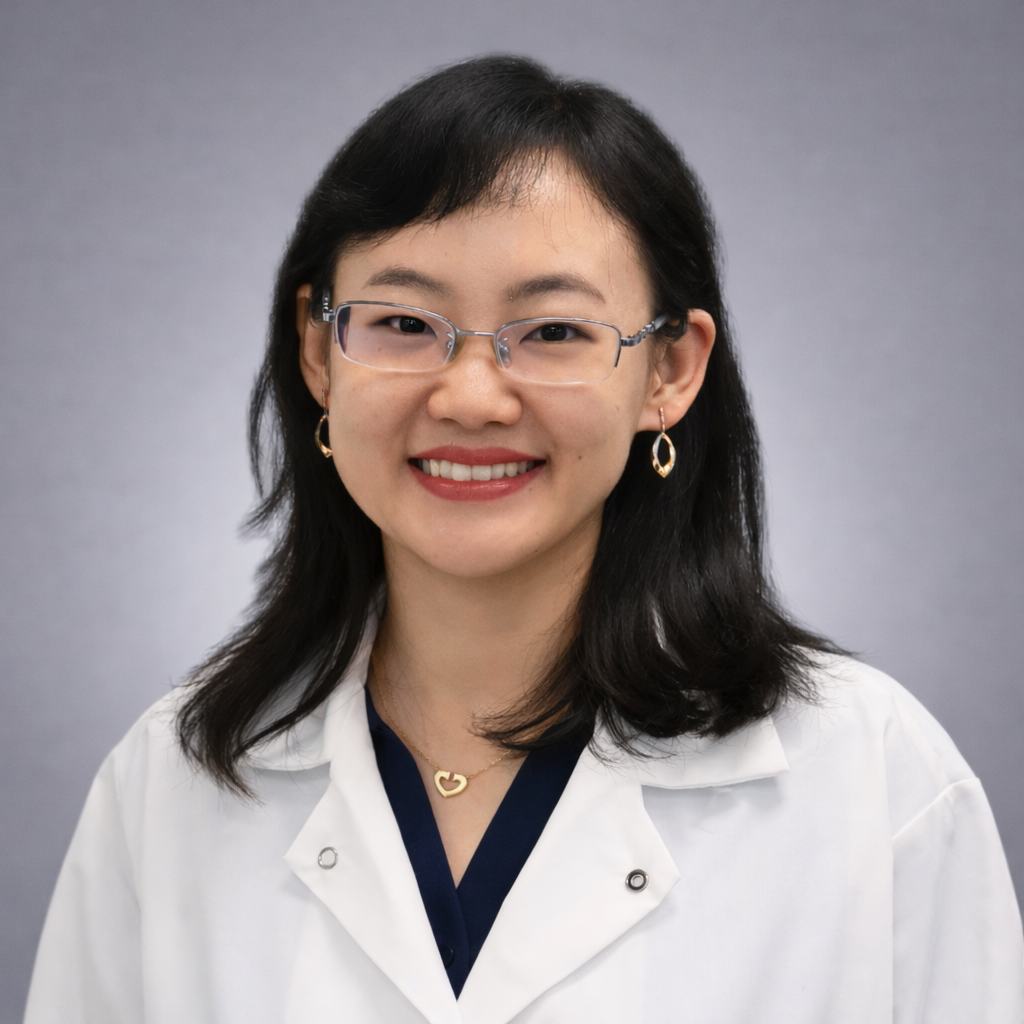 Headshot of Dr. Dan Jin, Acupuncturist, wearing glasses and a white clinical coat over a navy top against a soft gray studio background.