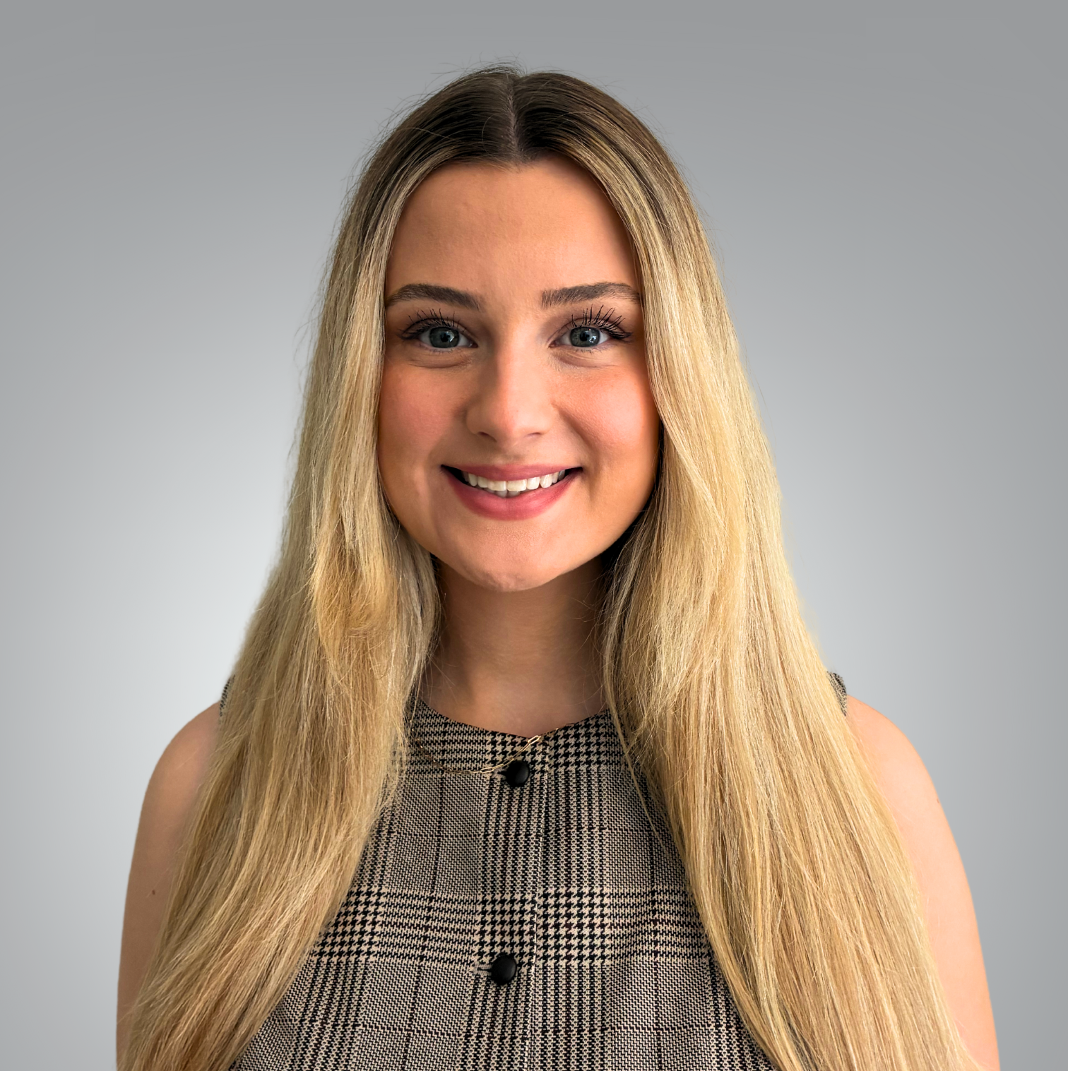 A professional headshot of Kathleen Stagg, Office Administrator and Patient Care Coordinator at Red Leaf Wellness, smiling with long blonde hair and wearing a plaid sleeveless top against a light gray background.