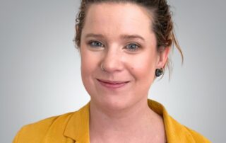 Portrait of Lia Crotenko, patient care coordinator, wearing a mustard jacket and smiling at the camera