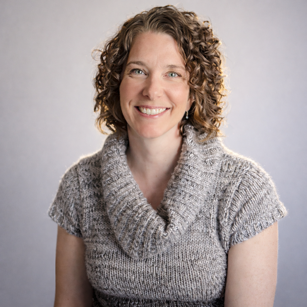 Headshot of Cora Rennie, Biodynamic Craniosacral Therapist, smiling gently in a gray cowl neck sweater against a soft gray studio background.