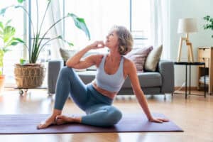 Middle-aged woman in athletic wear doing a seated yoga stretch on a mat at home, representing flexibility and exercise during perimenopause
