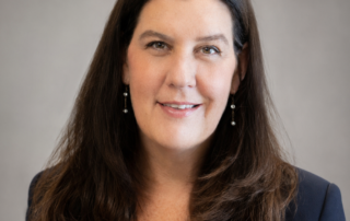 Professional headshot of Dr. Esnielle Brooks, Medical Director, smiling in a navy blazer against a soft gray studio background.
