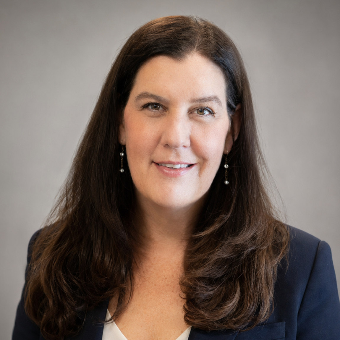 Professional headshot of Dr. Esnielle Brooks, Medical Director, smiling in a navy blazer against a soft gray studio background.