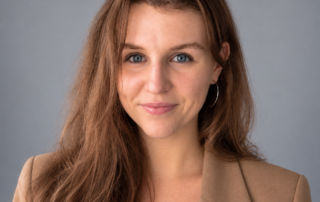 Professional headshot of Dr. Riley Forbes, ND, a naturopathic doctor focused on women’s health at Red Leaf Wellness, wearing a camel blazer against a soft gray background.