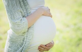 A pregnant person resting their hands above and below their belly outdoors.
