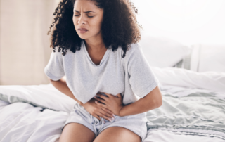 Woman seated on a bed holding her abdomen in discomfort
